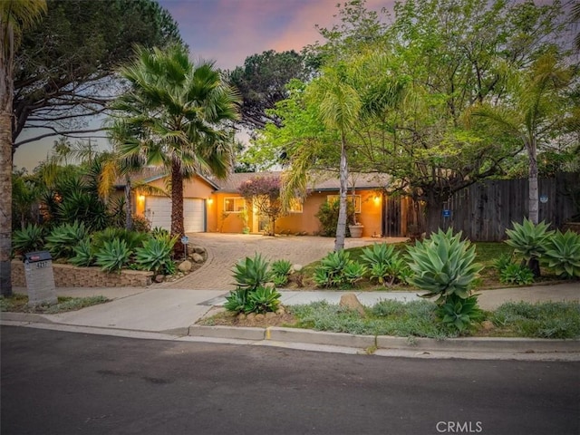 view of front facade with a garage, stucco siding, decorative driveway, and fence