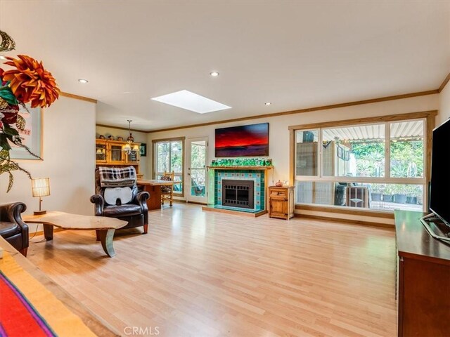 living room featuring recessed lighting, a tile fireplace, crown molding, a skylight, and light wood-style flooring