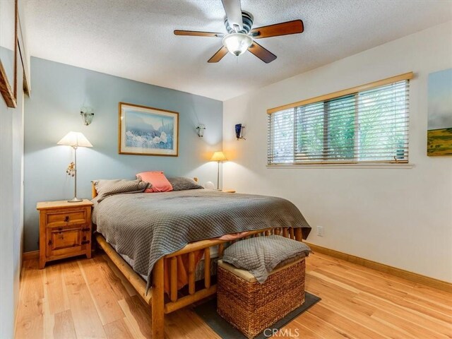 bedroom featuring light wood-style flooring, a textured ceiling, a ceiling fan, and baseboards