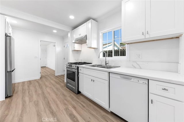 kitchen featuring white cabinets, a sink, crown molding, under cabinet range hood, and appliances with stainless steel finishes