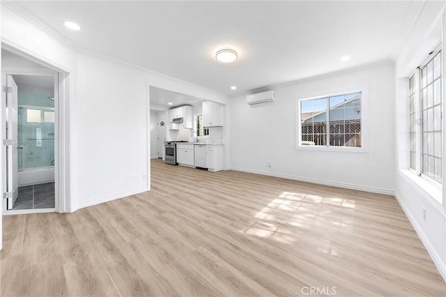 unfurnished living room with a wall mounted air conditioner, baseboards, ornamental molding, and light wood finished floors