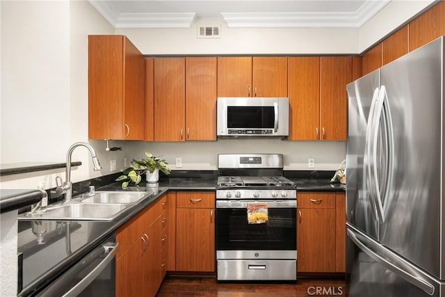 kitchen featuring appliances with stainless steel finishes, a sink, crown molding, dark wood-type flooring, and dark countertops