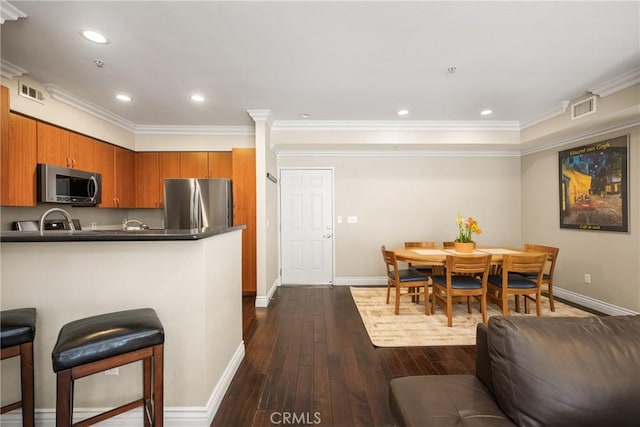 kitchen featuring stainless steel appliances, dark countertops, brown cabinetry, dark wood-type flooring, and baseboards