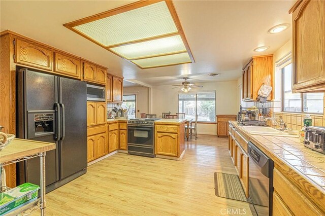 kitchen featuring stainless steel appliances, a peninsula, light wood-type flooring, brown cabinets, and tile countertops