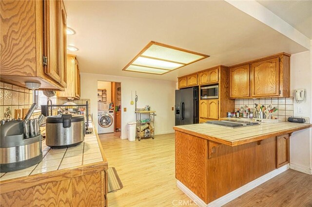 kitchen featuring stainless steel microwave, washer / dryer, tile countertops, and black fridge