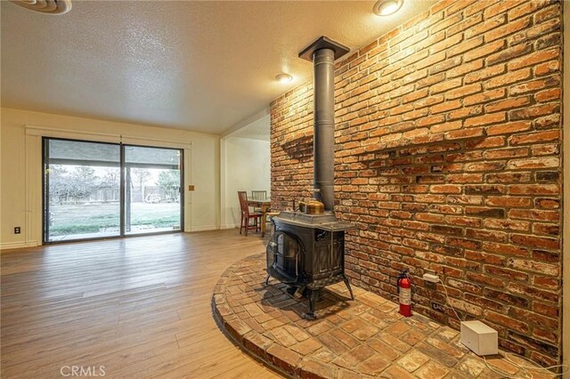 living room with brick wall, baseboards, a textured ceiling, and a wood stove
