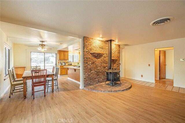 living room with a textured ceiling, light wood-type flooring, visible vents, a ceiling fan, and a wood stove
