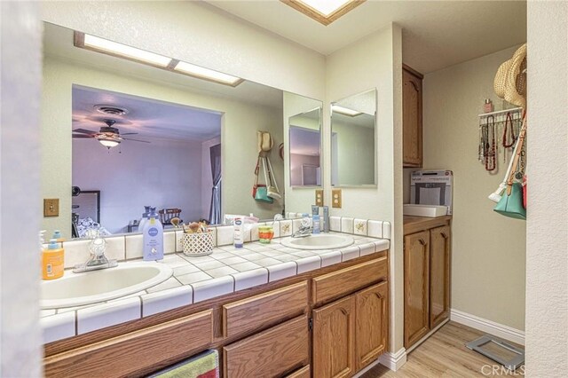 bathroom with a ceiling fan, wood finished floors, a sink, and double vanity