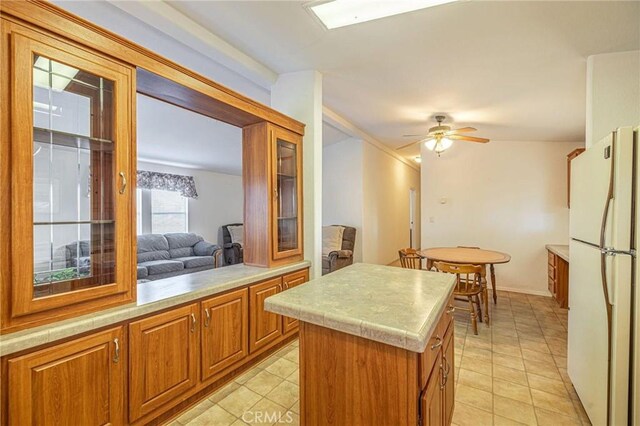kitchen with freestanding refrigerator, brown cabinets, light countertops, a kitchen island, and light tile patterned floors