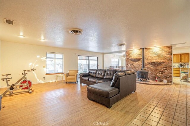 living room with a textured ceiling, light wood-type flooring, a wood stove, and visible vents