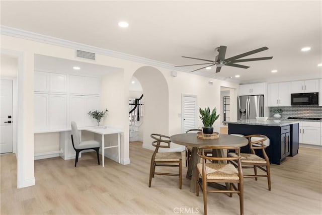 dining space featuring ceiling fan, light wood-type flooring, visible vents, ornamental molding, and arched walkways