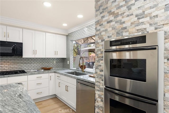kitchen featuring white cabinets, a sink, light stone countertops, crown molding, and black appliances