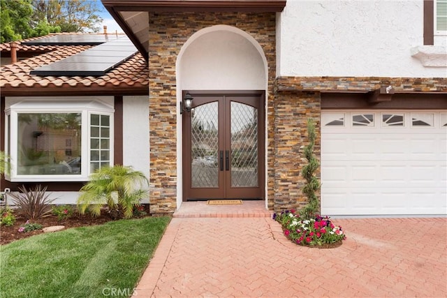 doorway to property featuring a tiled roof, french doors, a garage, stucco siding, and solar panels