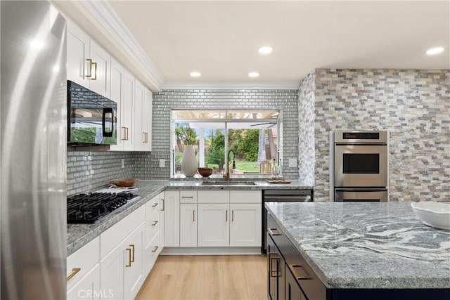 kitchen with stainless steel appliances, a sink, white cabinetry, and crown molding