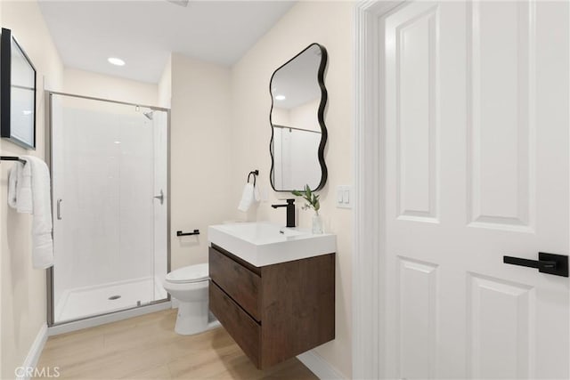 bathroom with toilet, baseboards, wood finished floors, a shower stall, and vanity