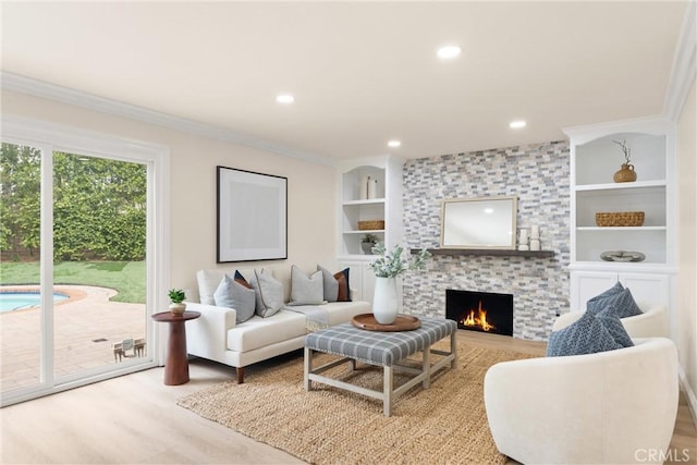 living room featuring crown molding, wood finished floors, built in shelves, a large fireplace, and recessed lighting