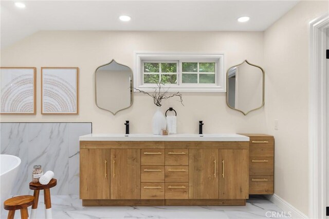 full bath with a sink, double vanity, a freestanding bath, recessed lighting, and marble finish floor