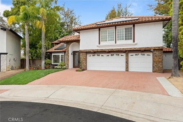 mediterranean / spanish home with a garage, decorative driveway, a tiled roof, solar panels, and stucco siding