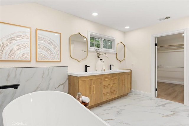 bathroom with marble finish floor, double vanity, visible vents, a sink, and a soaking tub