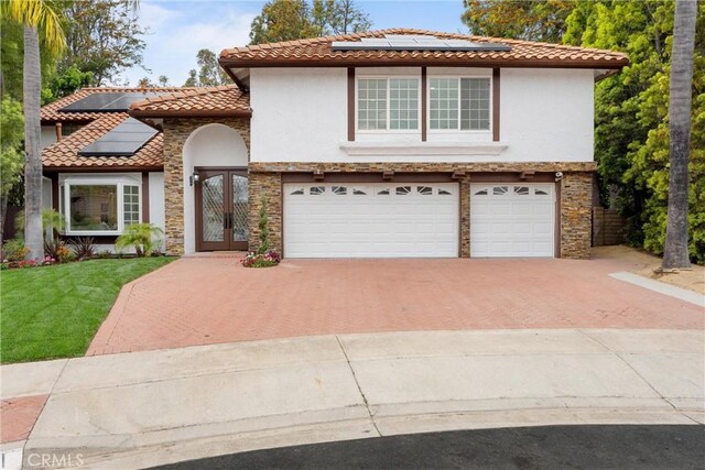 view of front of home with french doors, an attached garage, roof mounted solar panels, stucco siding, and decorative driveway