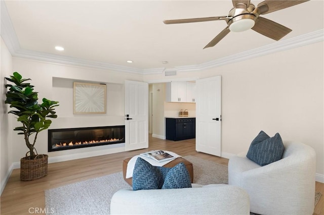 living area with a glass covered fireplace, ornamental molding, light wood finished floors, and baseboards