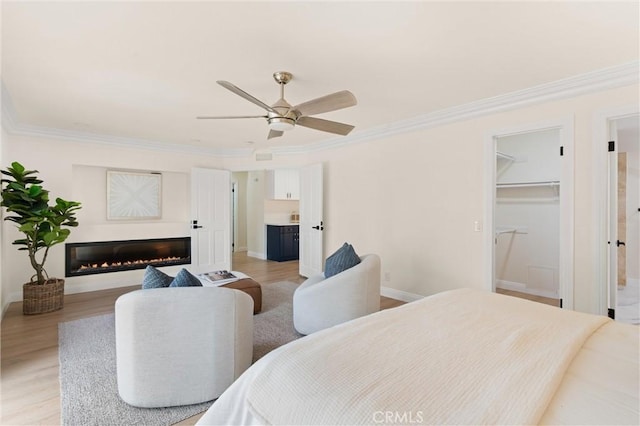 bedroom with ensuite bathroom, a glass covered fireplace, baseboards, light wood-type flooring, and crown molding