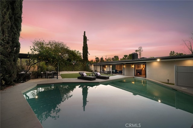 pool at dusk with outdoor lounge area, an outdoor pool, and a patio