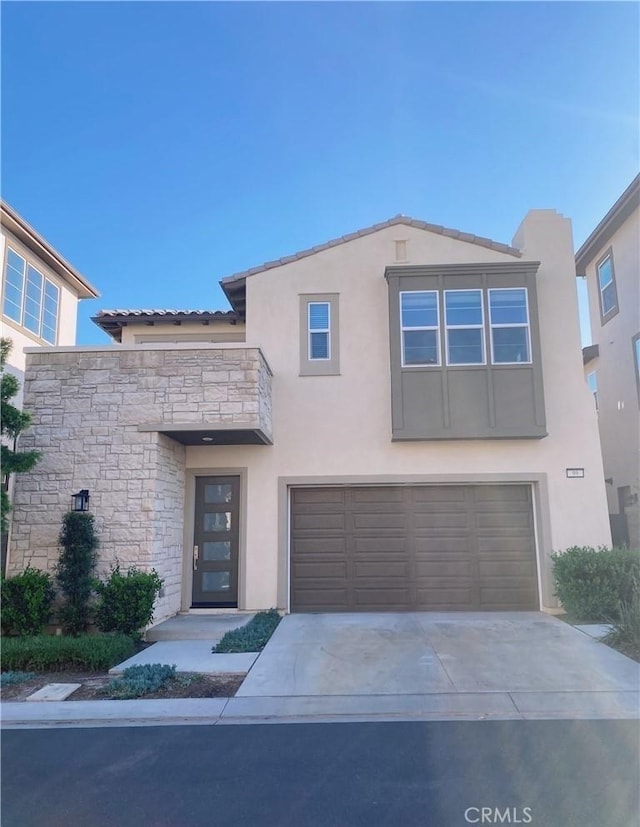 view of front of home featuring a garage, driveway, stone siding, and stucco siding