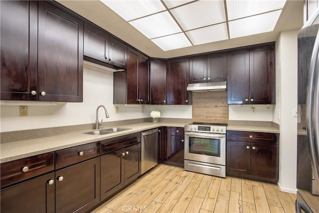 kitchen featuring under cabinet range hood, stainless steel appliances, light countertops, a sink, and light wood-type flooring