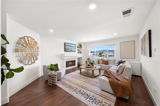 living area featuring wood finished floors, a warm lit fireplace, baseboards, and recessed lighting