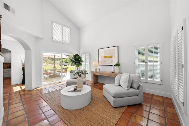 living area with high vaulted ceiling, arched walkways, tile patterned floors, and baseboards