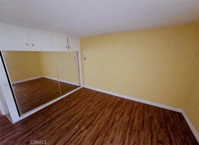 unfurnished bedroom featuring wood finished floors, a closet, and baseboards