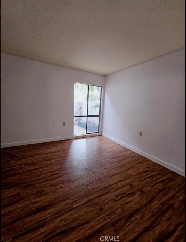 unfurnished room with baseboards, a textured ceiling, and dark wood-style floors