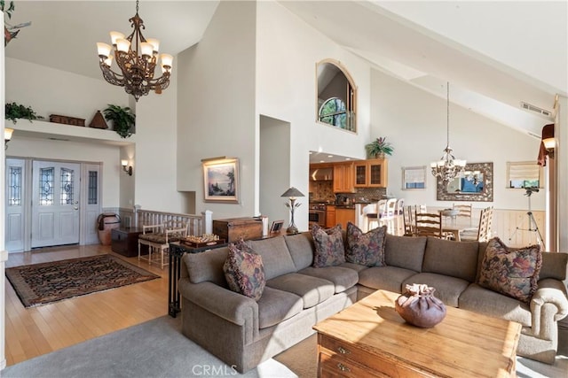 living area featuring high vaulted ceiling, an inviting chandelier, wood finished floors, and visible vents