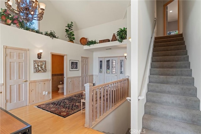 stairway featuring an inviting chandelier, a wainscoted wall, wood finished floors, and high vaulted ceiling