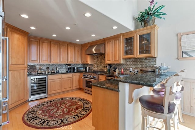 kitchen featuring wall chimney range hood, dark stone countertops, high end range, beverage cooler, and a peninsula