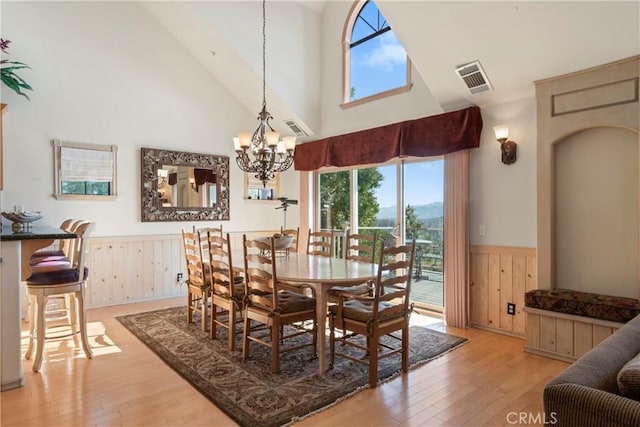 dining room featuring an inviting chandelier, wooden walls, a wainscoted wall, and light wood finished floors