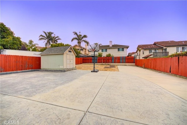 patio terrace at dusk featuring a fenced backyard, an outdoor structure, and a shed