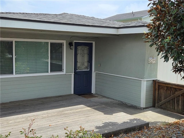 entrance to property with a wooden deck and roof with shingles