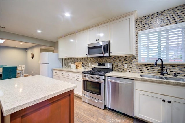 kitchen featuring light wood finished floors, a sink, appliances with stainless steel finishes, and tasteful backsplash