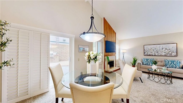 dining space featuring a glass covered fireplace, carpet floors, and high vaulted ceiling