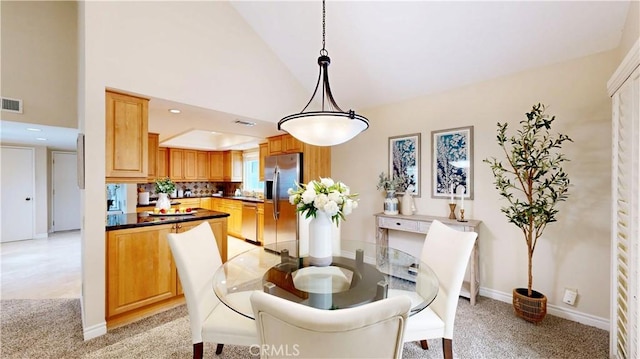 dining room with visible vents, baseboards, high vaulted ceiling, and light colored carpet