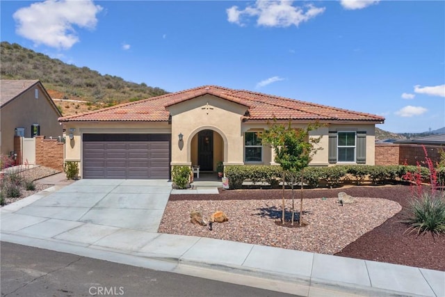 mediterranean / spanish house with concrete driveway, an attached garage, a tile roof, and stucco siding