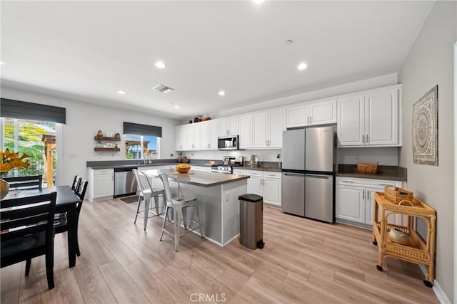 kitchen featuring white cabinets, dark countertops, appliances with stainless steel finishes, and light wood-style flooring
