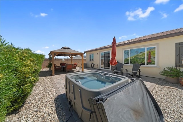 rear view of house featuring a fenced backyard, stucco siding, a patio area, a gazebo, and a hot tub