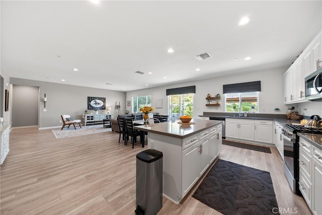 kitchen featuring dark countertops, a center island, light wood-type flooring, white cabinets, and stainless steel appliances