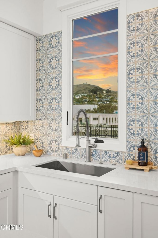 kitchen featuring decorative backsplash, white cabinetry, a sink, and light countertops