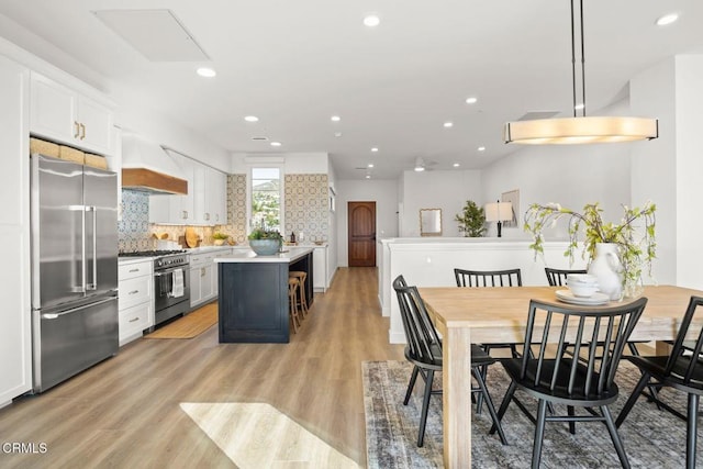interior space with premium appliances, light wood-style floors, custom range hood, white cabinetry, and recessed lighting