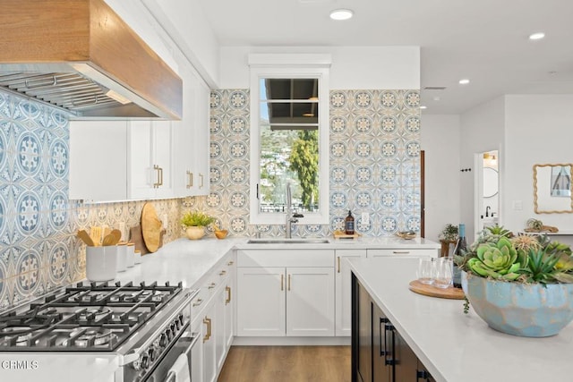 kitchen with custom exhaust hood, a sink, stainless steel gas range, light countertops, and white cabinetry