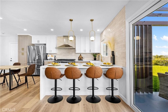kitchen featuring light countertops, wall chimney range hood, light wood-style floors, stainless steel fridge, and range